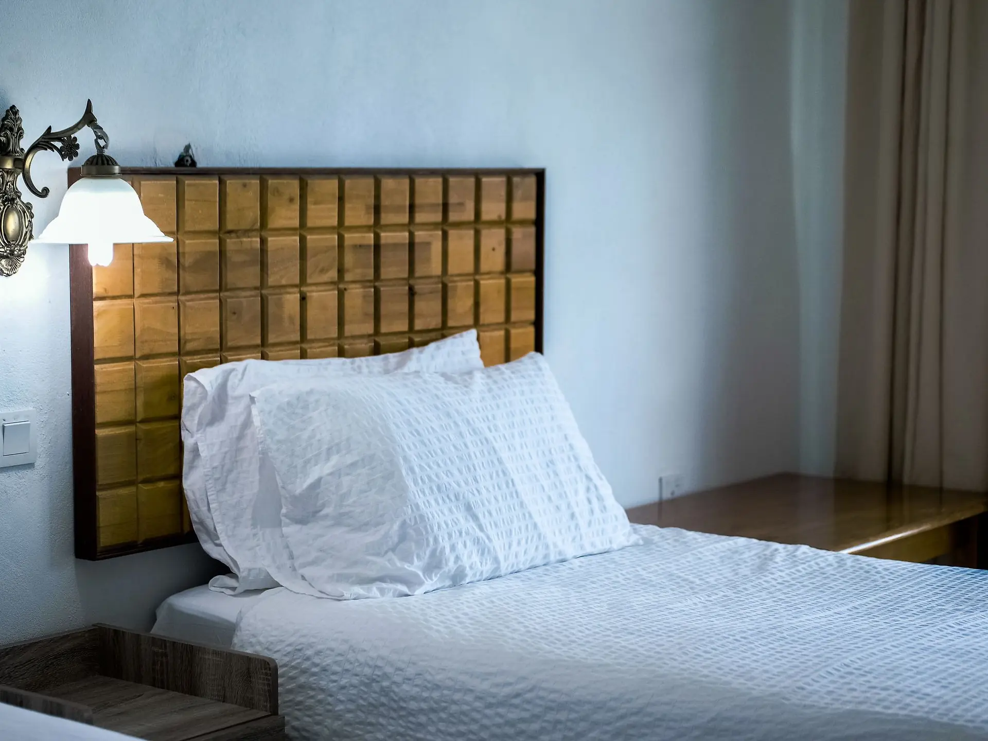 Wooden side table beside a made bed